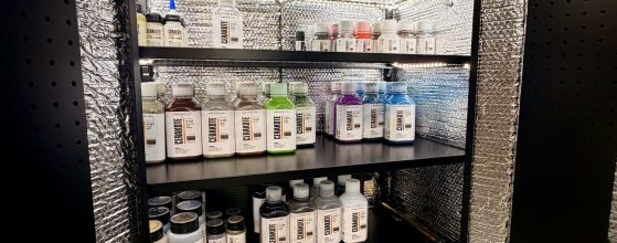 Colorful ceramic coating bottles on black shelving unit, automotive and firearm finishes.